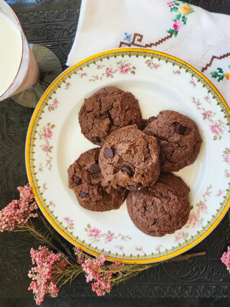 Chocolate peanut butter cookies on a china plate with milk, flowers, and a napkin