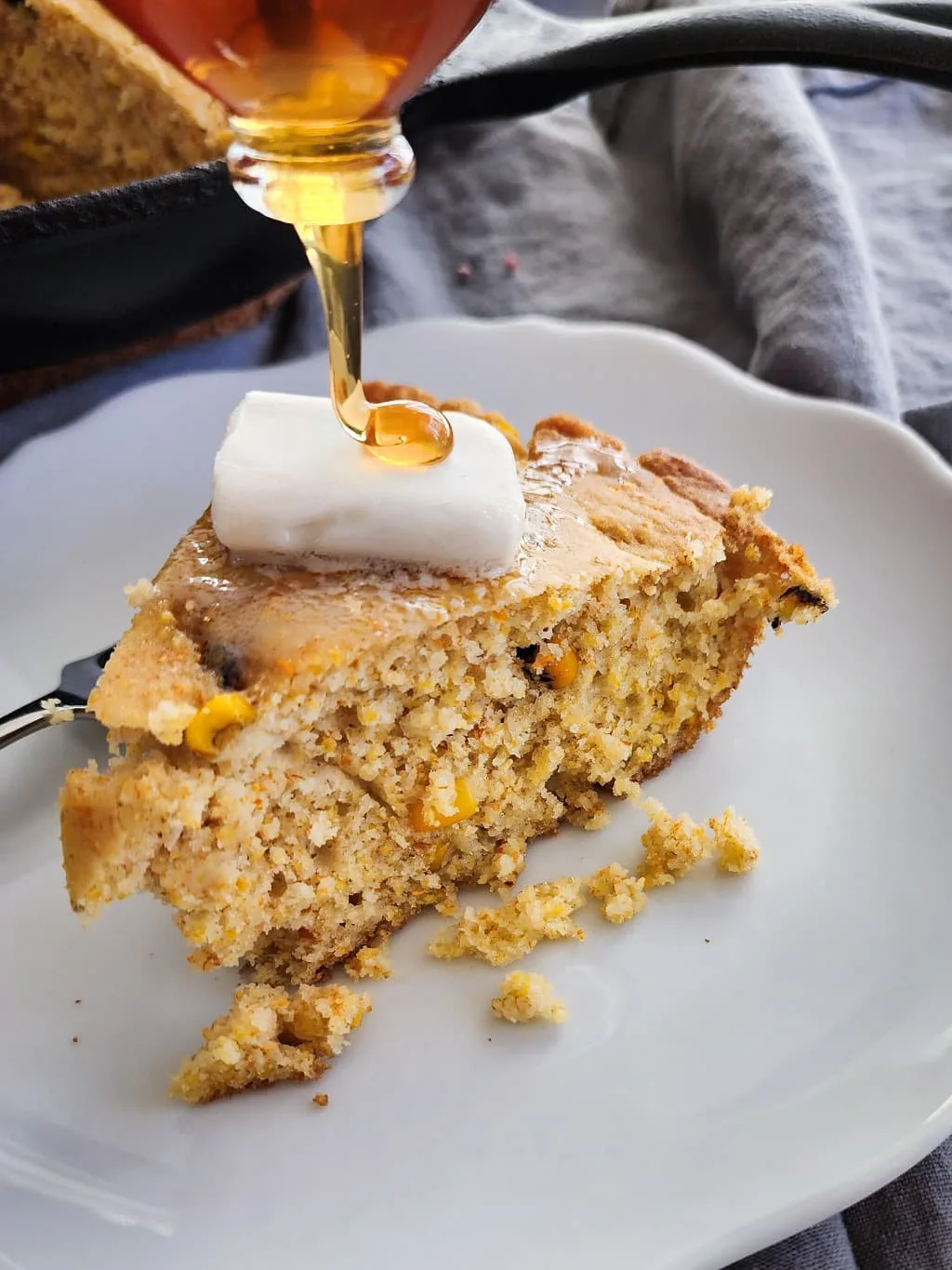 A serving of gluten free cornbread on a plate with dairy free butter and honey